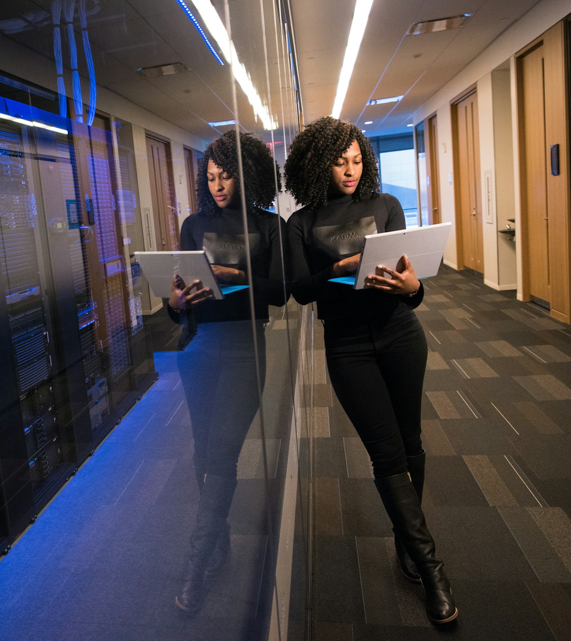 A woman in tech reviewing work on a laptop beside a wall of server racks